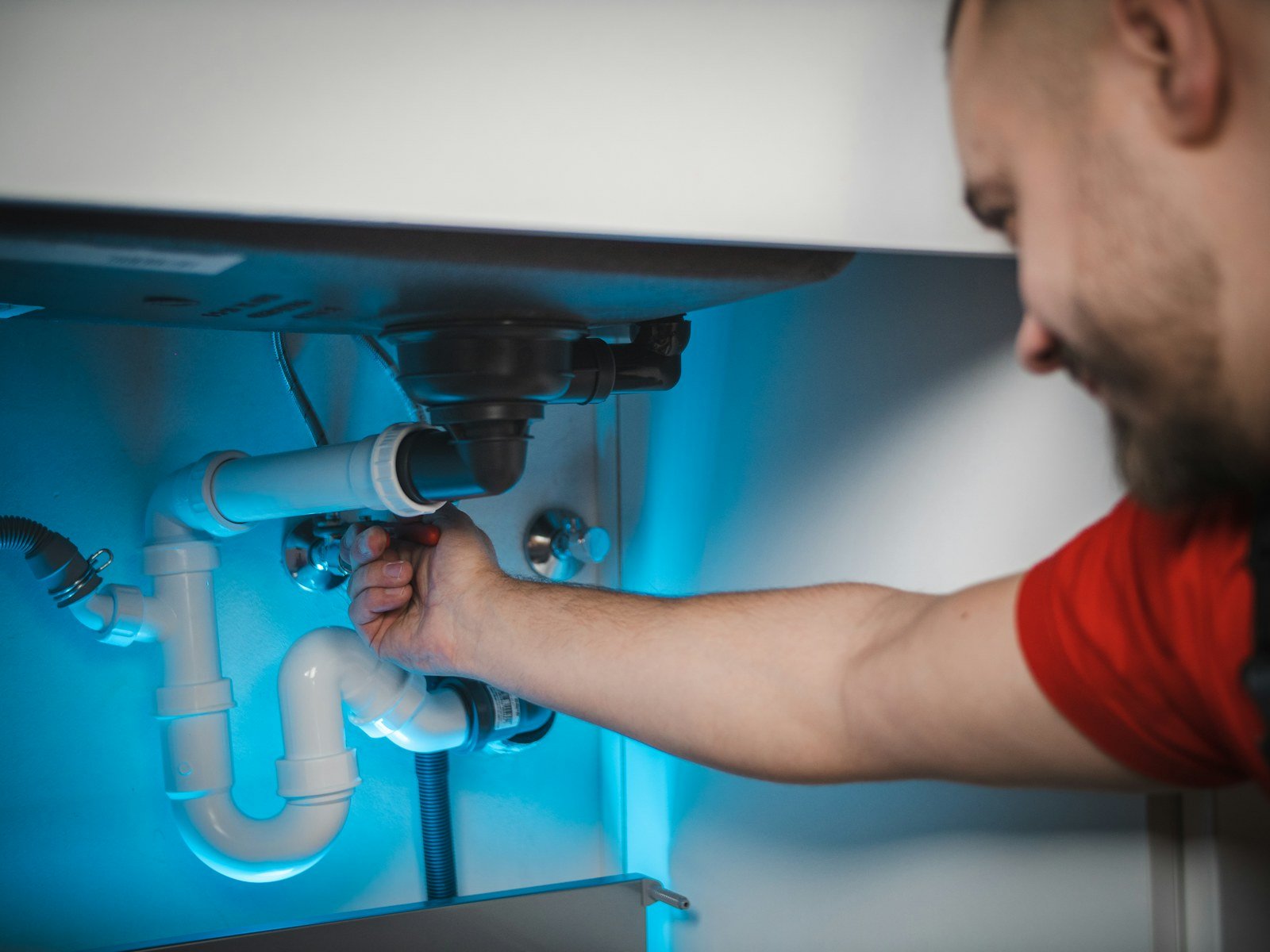 Close-up of a plumber's hands repairing exposed pipes beneath a sink during an emergency call