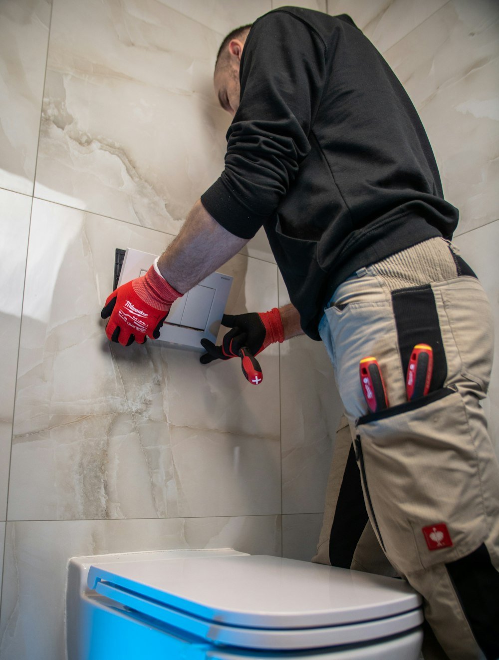 FlowGuard Plumbing technician in protective gloves repairing a bathroom fixture against a marble tile wall