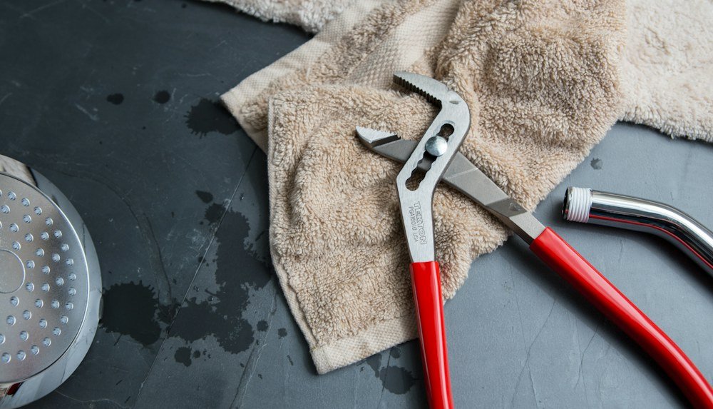 Drain cleaning pliers and a showerhead laid out on a service towel