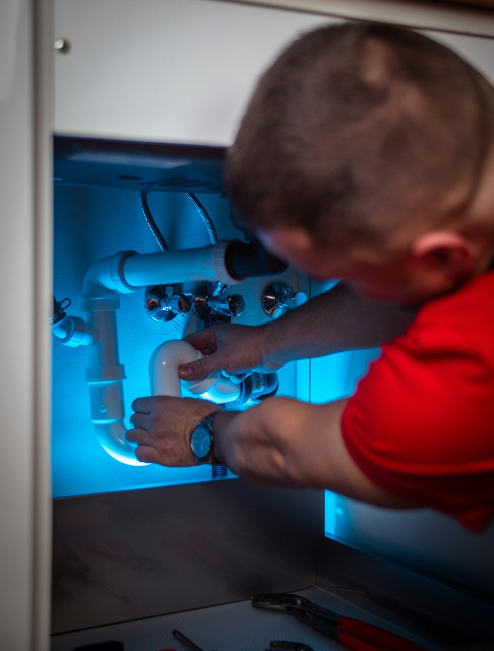 Plumber reaching into a cabinet to make an urgent pipe repair beneath a sink