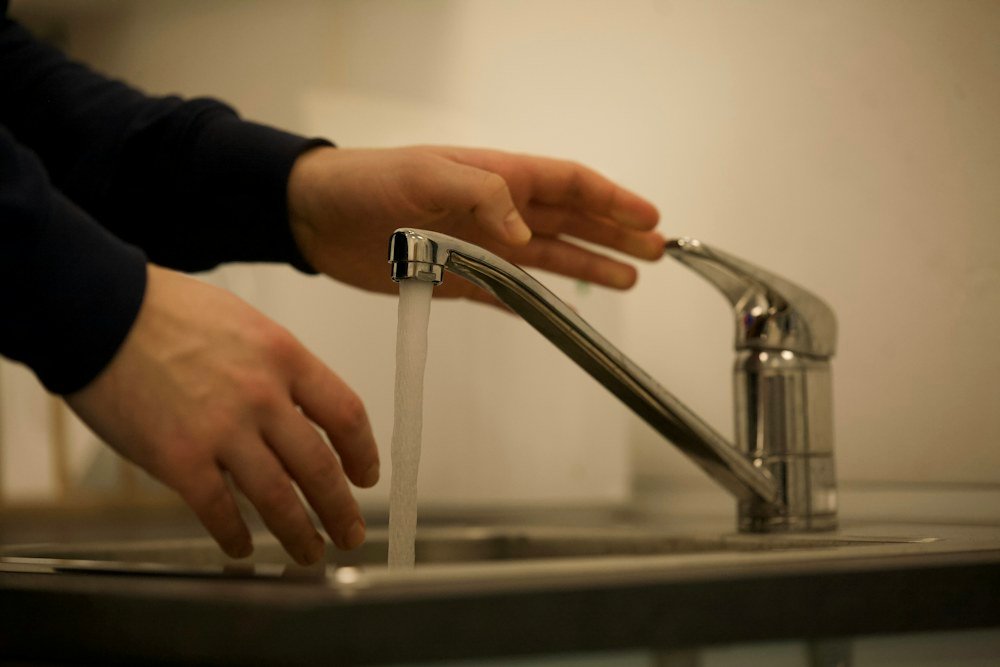 Technician testing water flow and pressure at a chrome faucet to check for hidden leaks