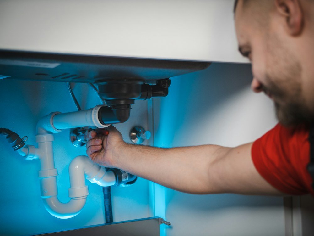 Plumber working with hands and tools on a pipe fitting inside a wall cavity