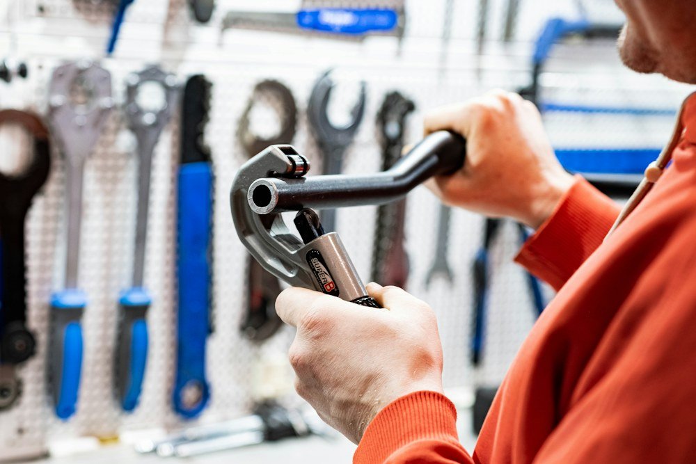 Plumber using a pipe cutting tool in front of a wall-mounted rack of wrenches